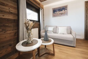 Una sala de estar con un muro de madera, un sofá, dos mesitas auxiliares y un cartel en la pared.