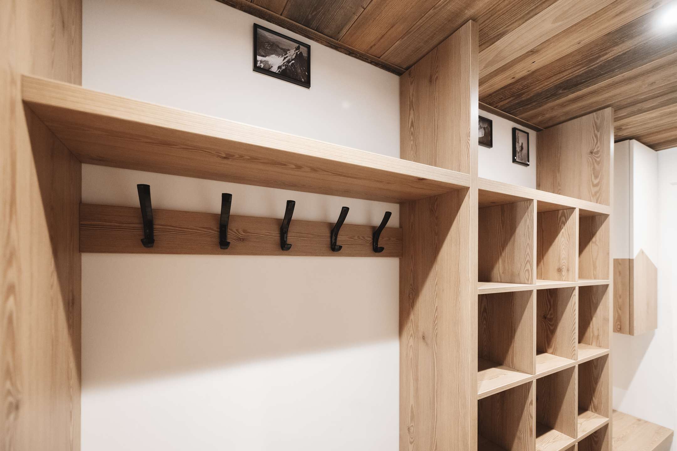 A wooden coat rack with hooks and a wooden shelving unit in a room with white walls and a wooden ceiling.