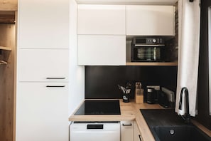 Eine kleine Küche mit weißen Schränken, einer schwarzen Induktionskochplatte, einem Backofen und einem Geschirrspüler.