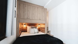 Un dormitorio con cabecera de madera, cama con ropa blanca y dos lámparas fijadas a la pared.