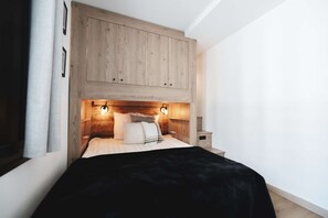 Un dormitorio con cabecera de madera, cama con ropa blanca y dos lámparas fijadas a la pared.