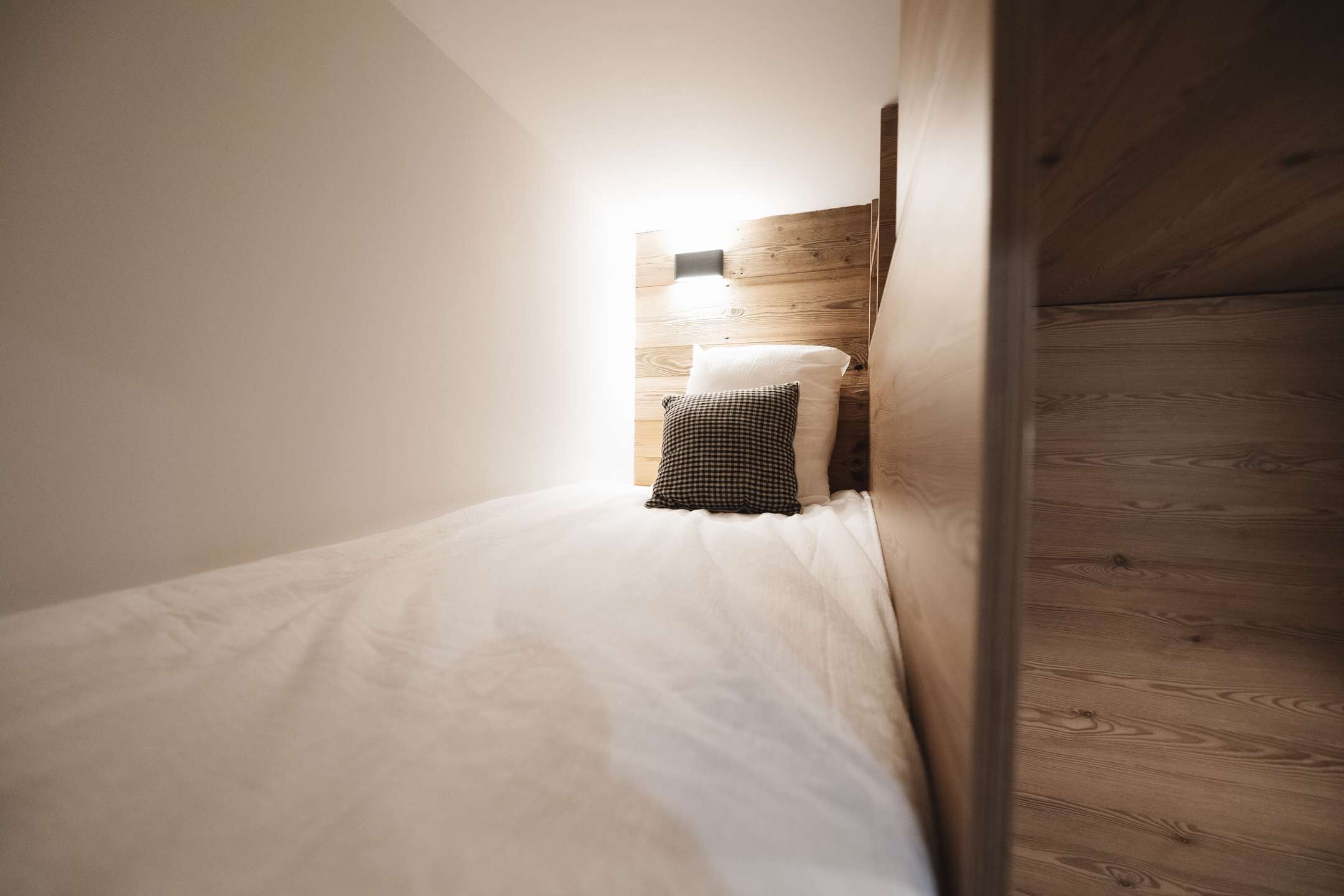 Une petite chambre avec un lit simple, une tête de lit en bois et une table de chevet avec une lampe.