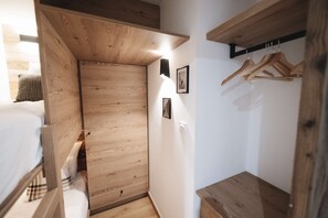 Een kleine kamer met een houten kledingkast, een bed en een klein tafeltje.