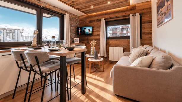 Una sala moderna con techo de madera, un comedor con sillas y mesa, un sofá y un televisor montado en la pared.