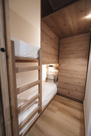 Ein kleiner, schmaler Raum mit einem Etagenbett, einem Nachttisch mit Lampe und Holzwänden.