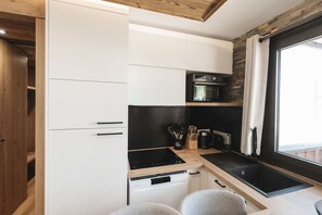 Una cocina compacta con armarios blancos, encimera negra y horno empotrado.