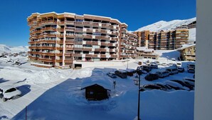 Hotel de varios pisos con balcones, rodeado de montañas nevadas y un estacionamiento.