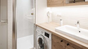 Un baño moderno con cabina de ducha de vidrio, lavadora integrada y tocador de madera con espejo.