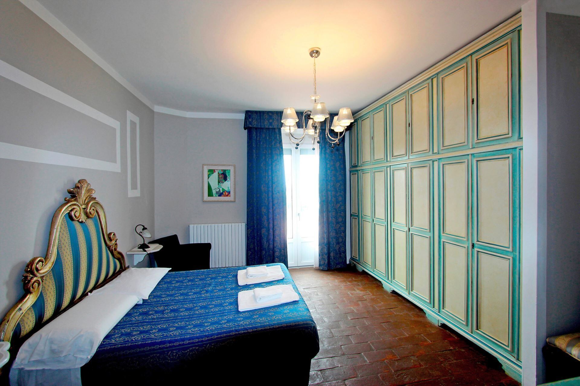 A bedroom with a large bed, a chandelier, a radiator, and a wardrobe.