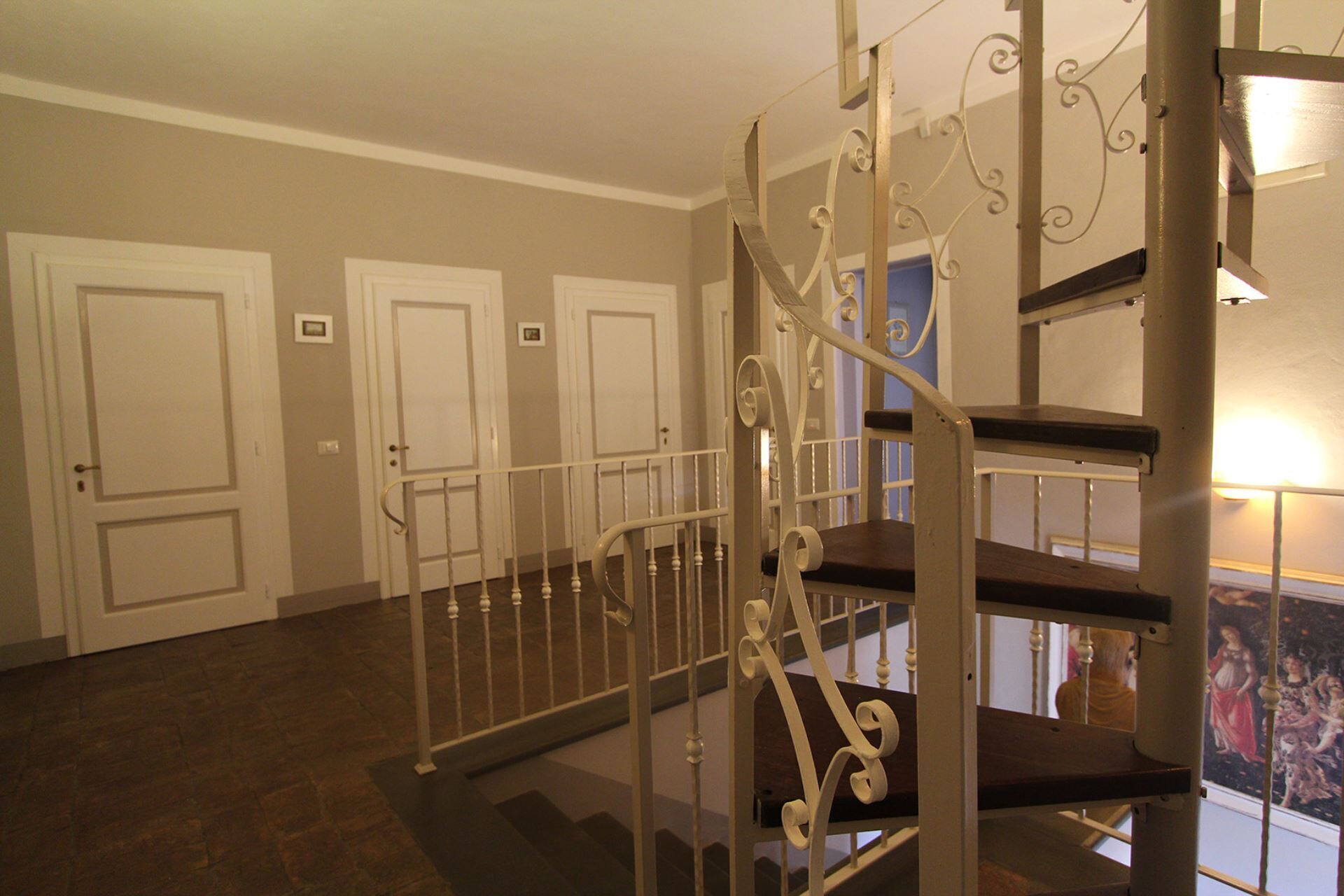 A staircase with ornate metal railings and a handrail, leading to a landing with a view of a balcony.