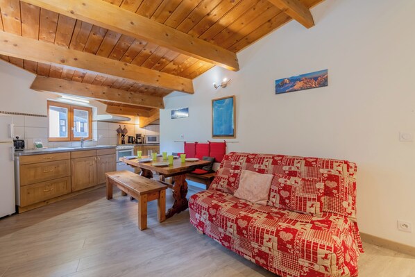 A cozy kitchen with wooden cabinets, a dining table, and a red patterned sofa. - Appartement Grand Roc 2, Argentière (Chamonix), France (Argentière (Chamonix))