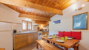 A kitchen with wooden cabinets, a wooden dining table with benches, and a red cushioned bench along the wall. - Appartement Grand Roc 2, Argentière (Chamonix), France (Argentière (Chamonix))