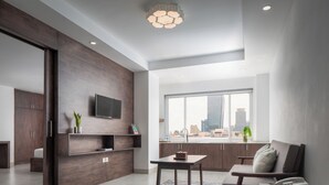 A modern living room with a large window, a flat-screen TV mounted on a wooden wall, a sofa, and a small table. - Vrest Hotel  (Phnom Penh)