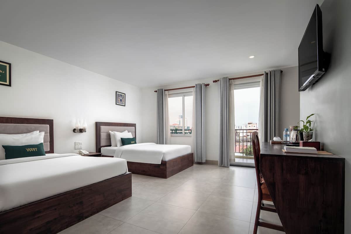 A hotel room with two beds, a desk, a chair, a TV, and a window with curtains.