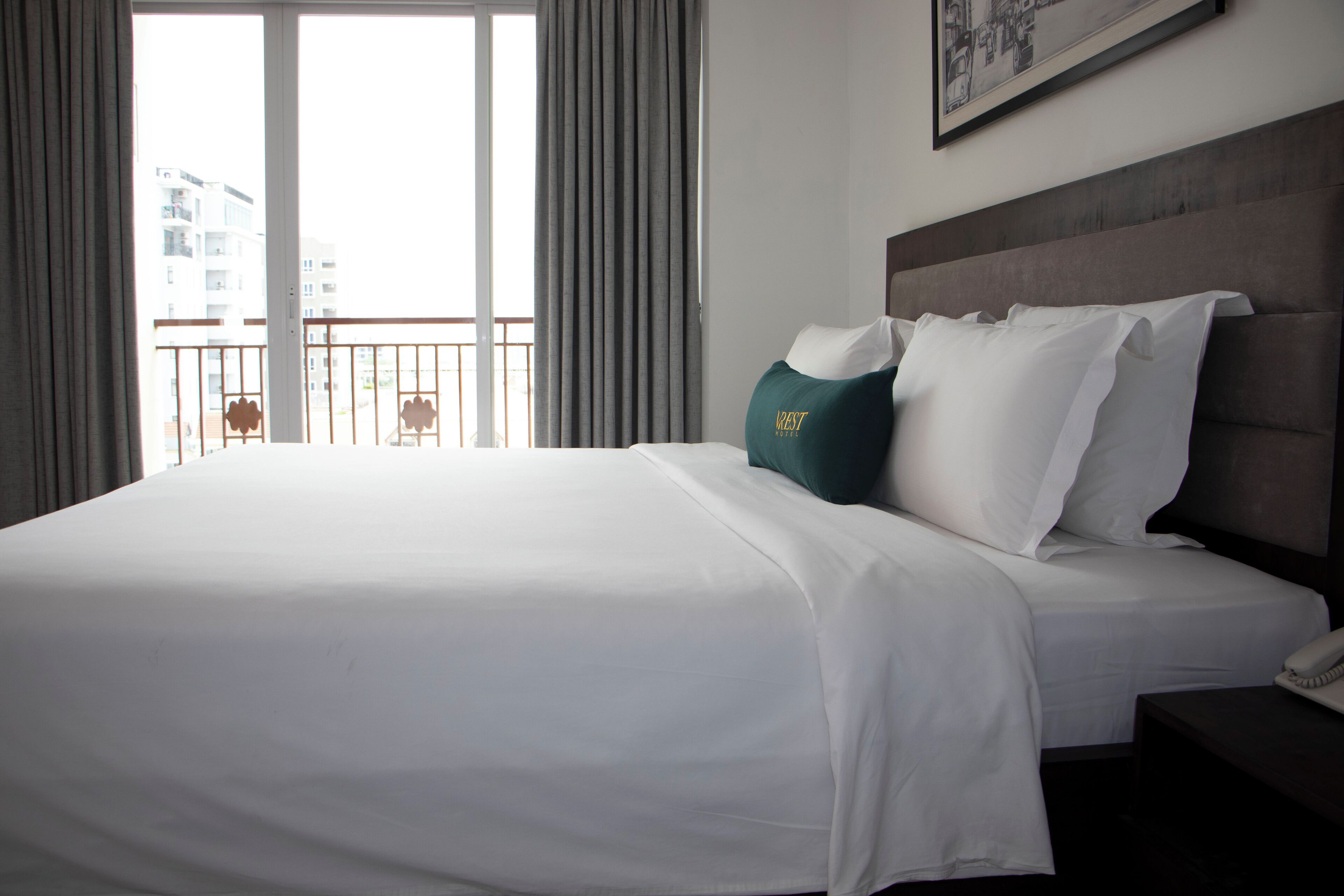 A hotel room with a large bed, a headboard, a bedside table, and a view of the outside balcony.