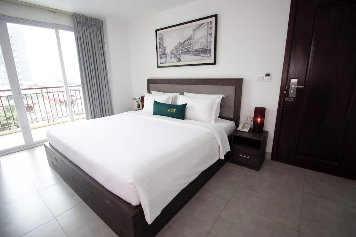 A hotel room with a large bed, a bedside table with a lamp, a framed picture on the wall, and a view of the outside through a sliding door.