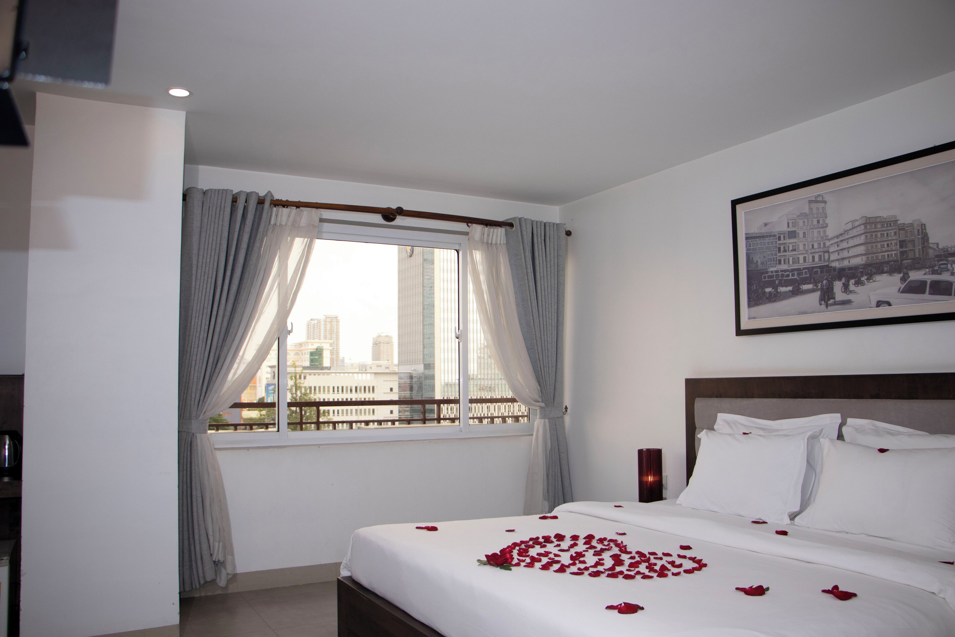 Une chambre d’hôtel avec un grand lit, une fenêtre avec des rideaux, un tableau encadré au mur et une vue sur la ville.