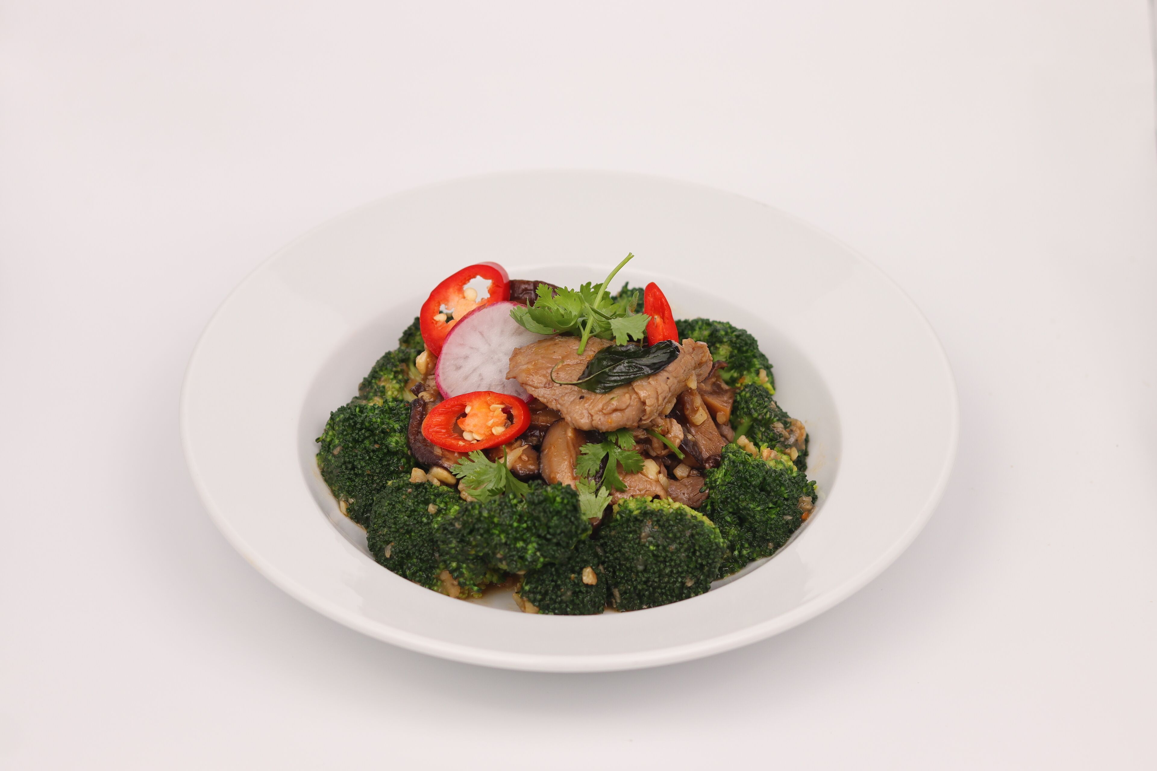 En vit tallrik med en måltid bestående av broccoli, skivade tomater, rädisor och svamp.