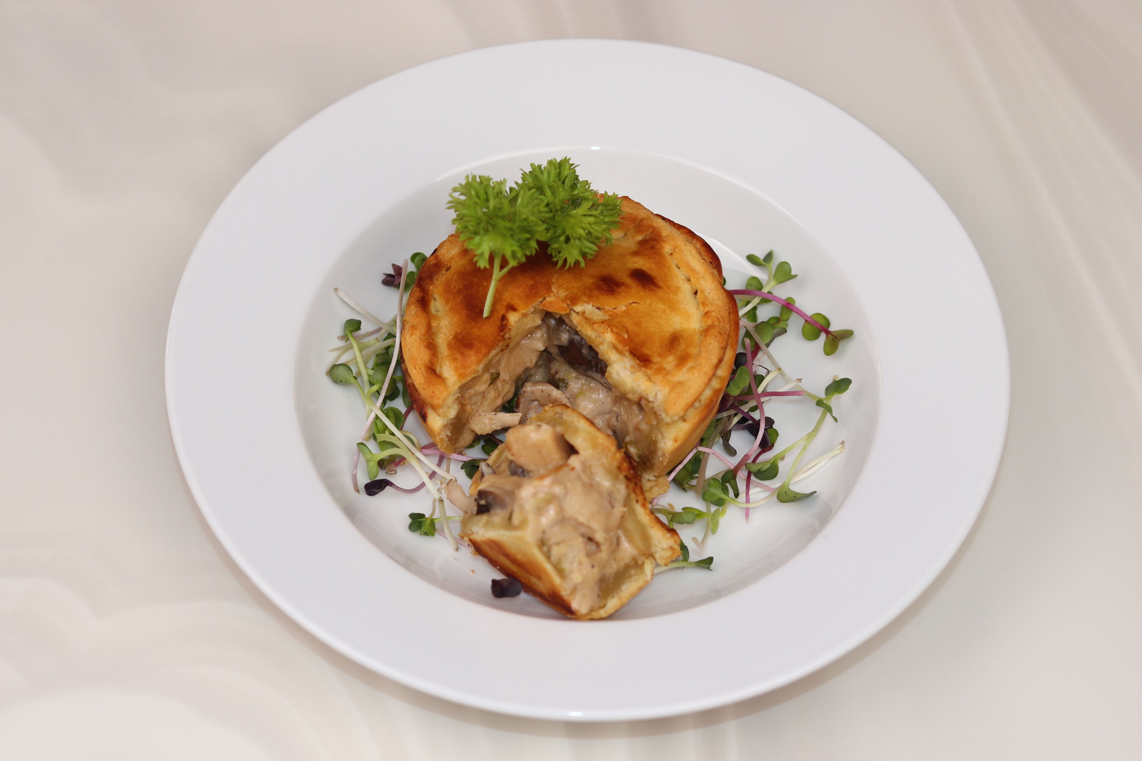 A white plate with a food item, possibly a pie, garnished with a sprig of parsley and surrounded by greens.