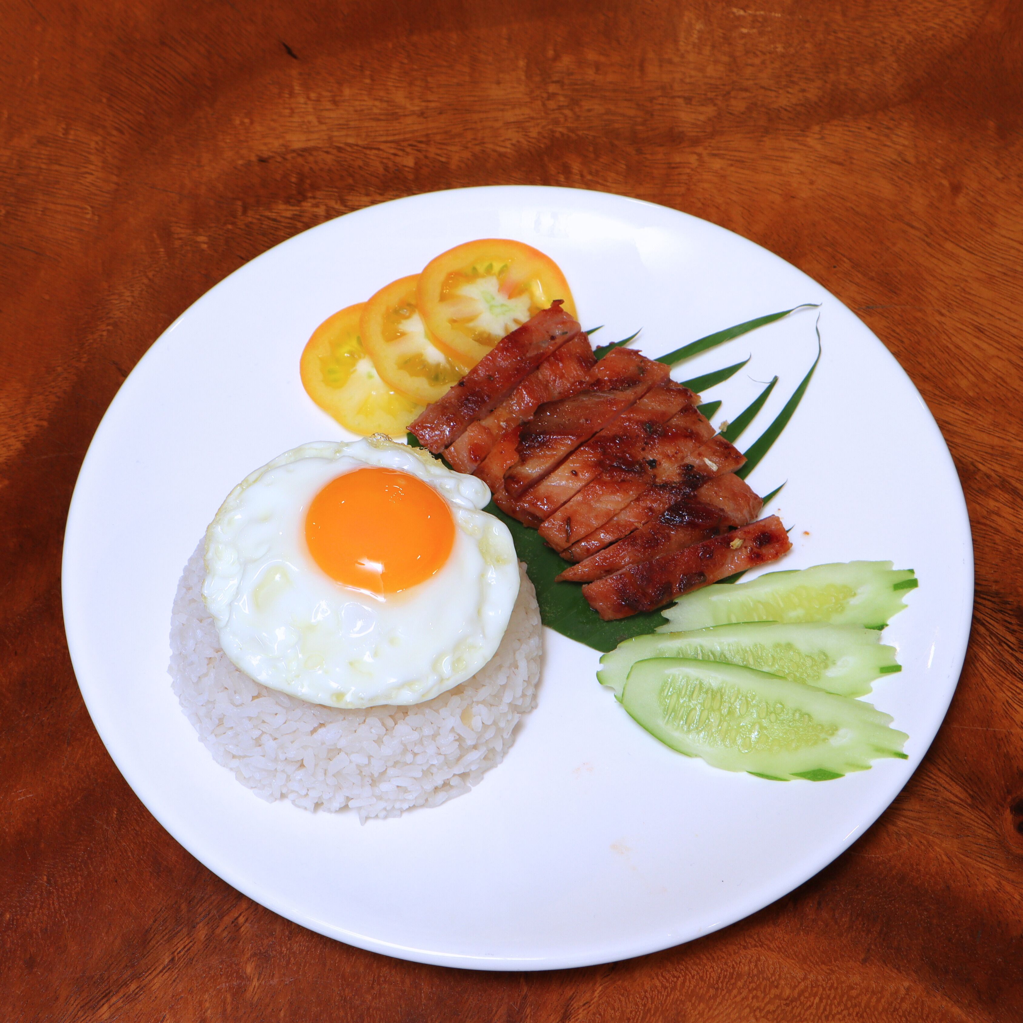 A plate with rice, a fried egg, slices of ham, tomato, and cucumber.