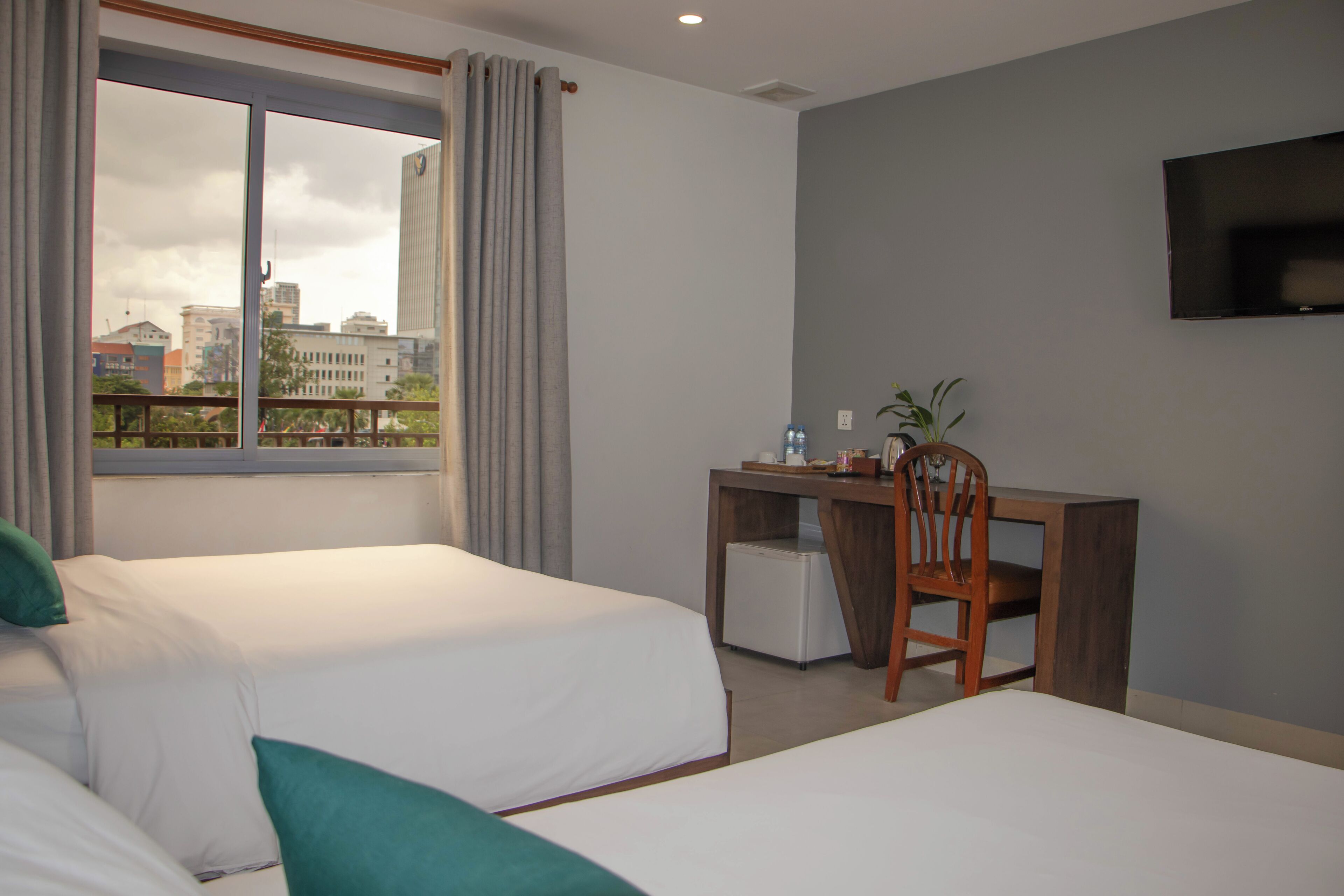 Une chambre d’hôtel avec deux lits, un bureau, une chaise, une télévision et une fenêtre avec des rideaux.