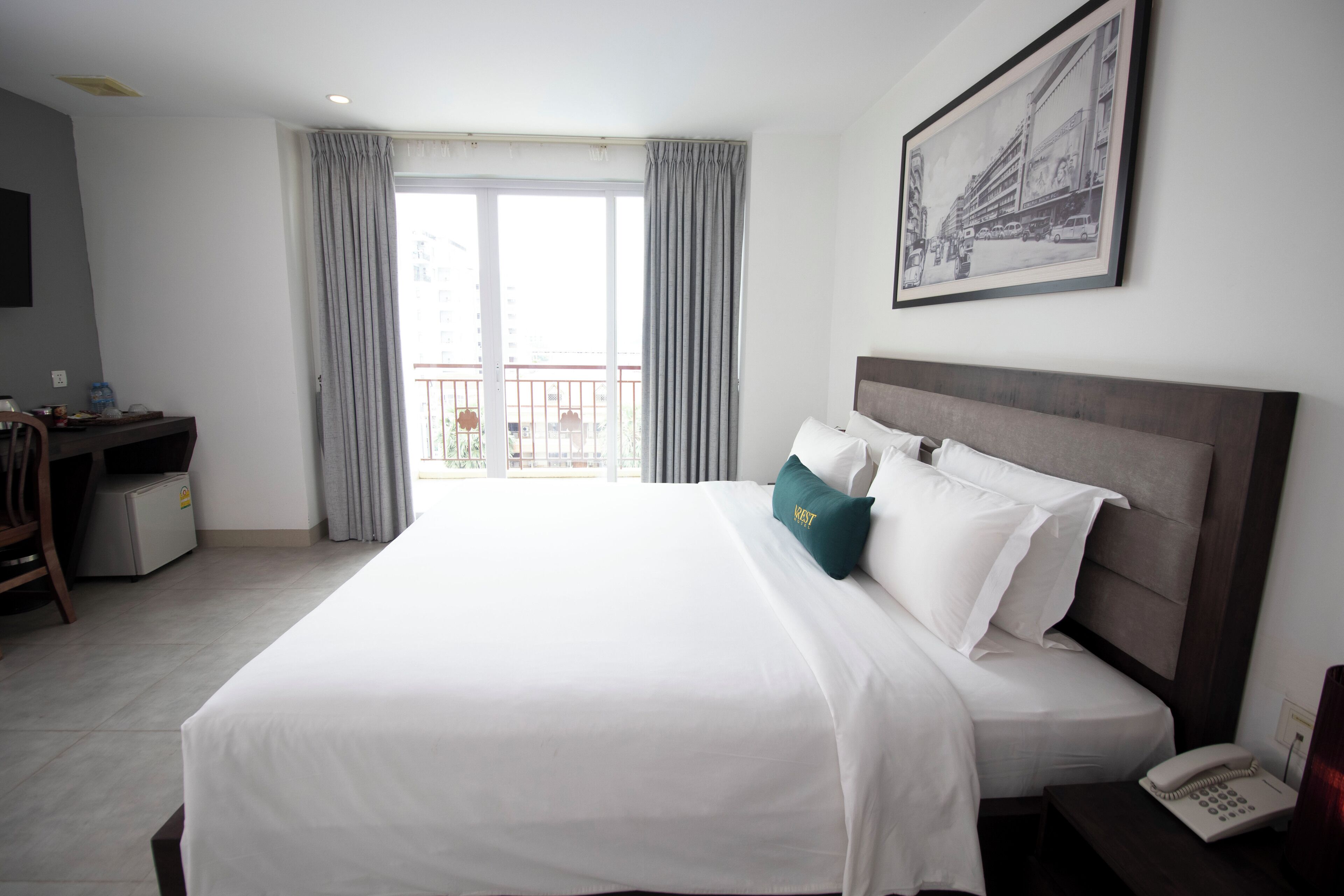 A hotel room with a large bed, a desk with a chair, a telephone, and a framed picture on the wall.
