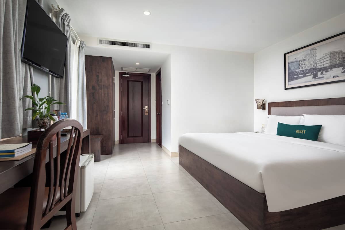 A hotel room with a bed, a desk with a chair, a TV, and a framed picture on the wall.