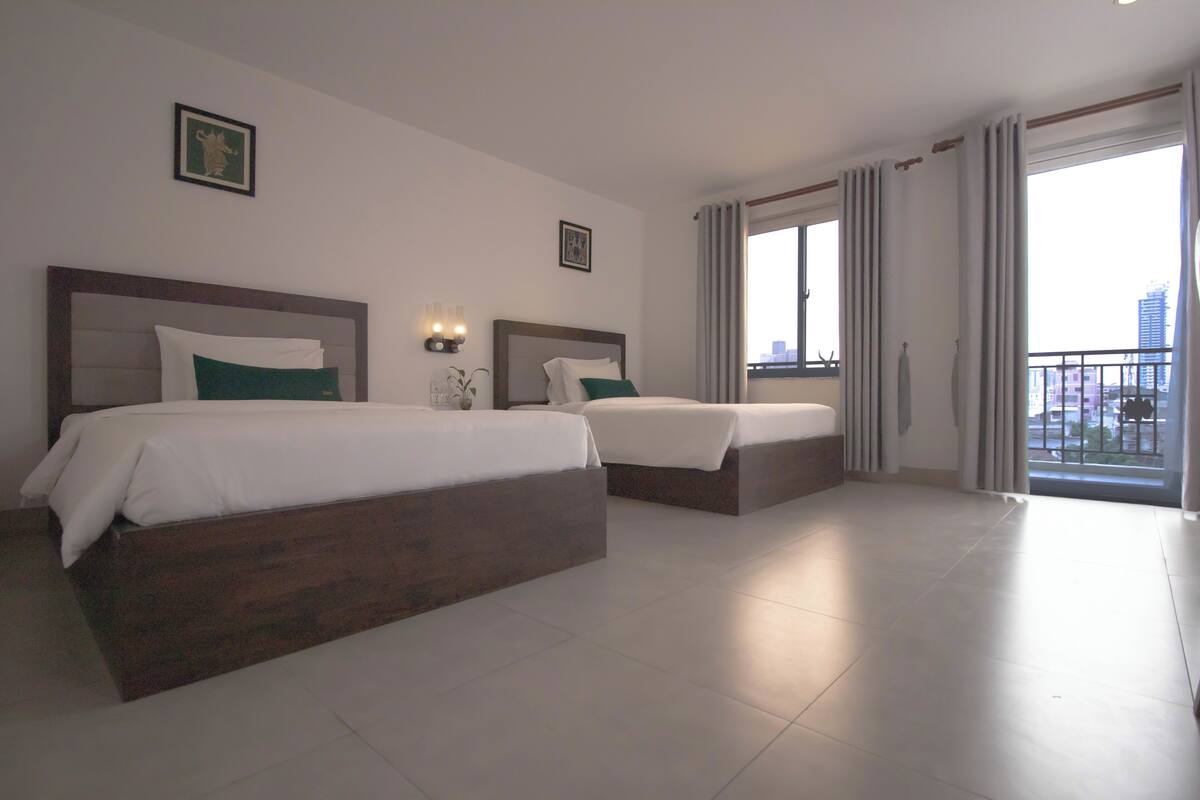 A hotel room with two beds, a balcony with curtains, and a city view.