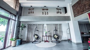 A spacious lobby with a high ceiling, a chandelier, a large window, and two unique hanging chairs. - Vrest Hotel  (Phnom Penh)