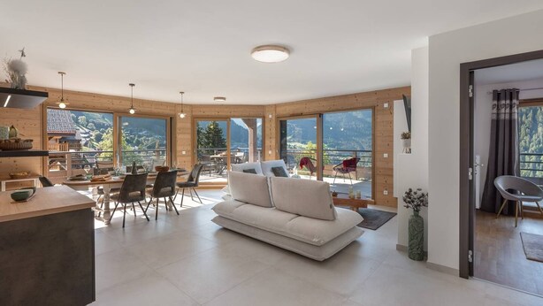 Un vaste espace de vie comprenant un canapé, une table à manger et des chaises. De grandes fenêtres offrent une vue sur l’extérieur.