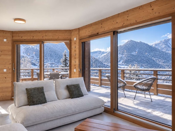 A cozy room with a sofa and chairs, large windows with a snowy mountain view.