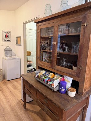 A kitchen with a wooden cabinet containing glassware and a drawer with food items.