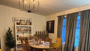 A dining area with a round table, wooden chairs, a chandelier, a cabinet with dishes, a Christmas tree, and a couch. - Country Escape on 32 Acres/Trough Pool, Hot Tub & Stunning Views (Dayton)