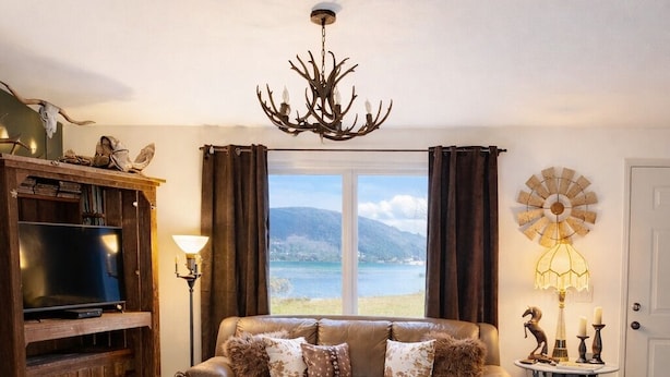 A cozy living room with a leather sofa, a wooden entertainment unit, a large window with a view, and a decorative windmill. - Country Escape on 32 Acres/Trough Pool, Hot Tub & Stunning Views (Dayton)