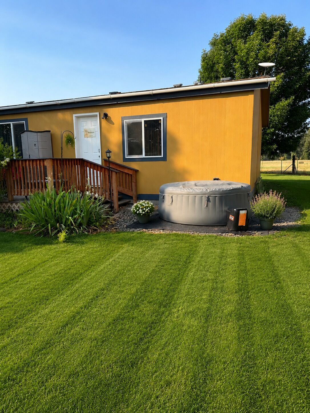 A single-story building with a wooden deck, a hot tub, and a well-maintained lawn.