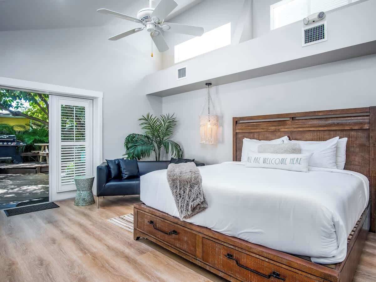 A bedroom with a large bed, a ceiling fan, and a view of the outdoors.