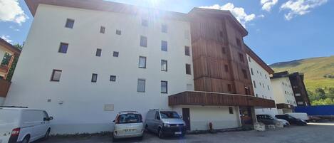 Un immeuble à plusieurs étages, doté d’une façade blanche et d’une partie en bois sur le côté droit. Plusieurs voitures sont garées devant.