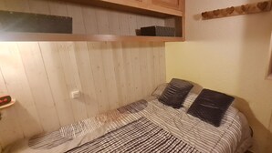 Ein kleines Zimmer mit einem Einzelbett, einem Holz-Lattenrost, einem Nachttisch und einem Regal über dem Bett.