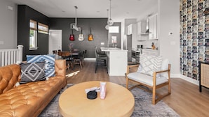 Una sala de estar moderna con un sofá de cuero marrón, una mesa de centro redonda y un comedor con una mesa y sillas blancas.
