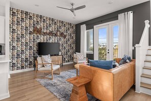 A living room with a patterned wallpaper, a flat-screen TV, a sofa, and a staircase.