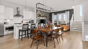 Una cocina moderna con armarios blancos, una isla central con asientos y un comedor con sillas de madera.