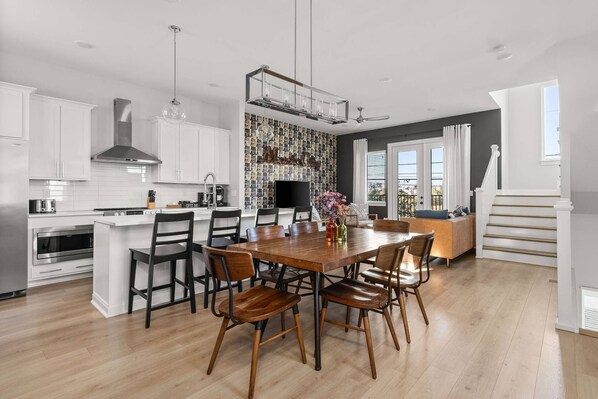 A modern kitchen with white cabinets, a central island with seating, and a dining area with wooden chairs.