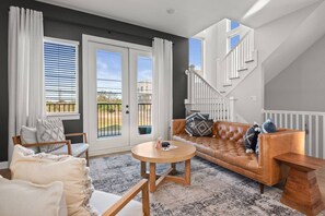 A modern living room with a leather sofa, a round wooden coffee table, and a staircase leading to an upper floor.