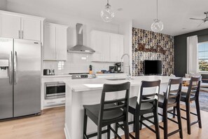 A modern kitchen with white cabinetry, a stainless steel refrigerator, a built-in oven, and a coffee station.