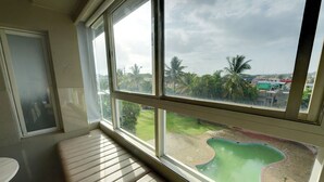 A room with a large window overlooking a swimming pool and palm trees. - Hotel Sankam Residency (Belagavi)