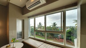 A room with a large window, a bench, and a small table with a vase and plates. - Hotel Sankam Residency (Belagavi)