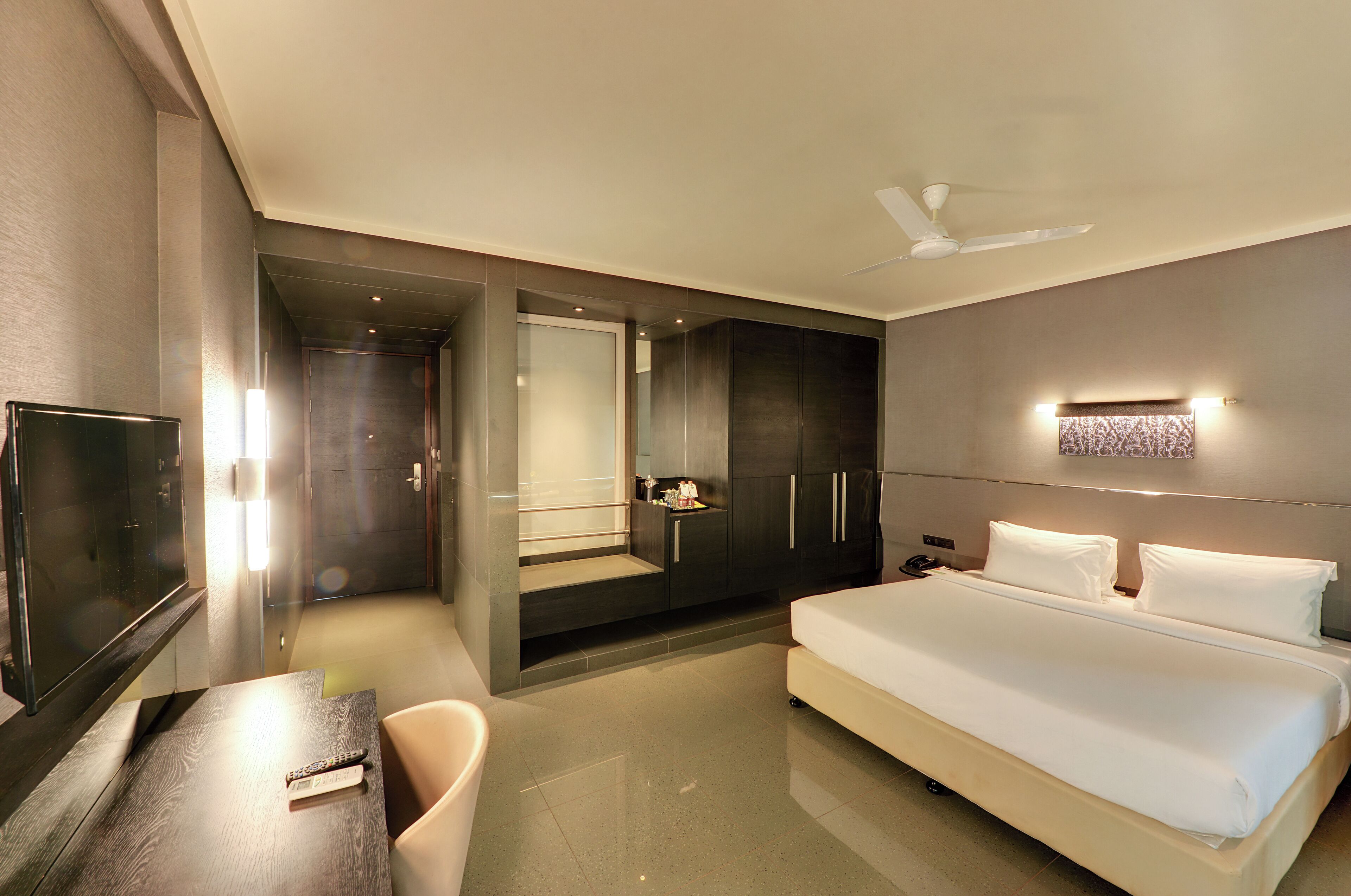 A modern hotel room with a large bed, a desk, a TV, and a wardrobe.