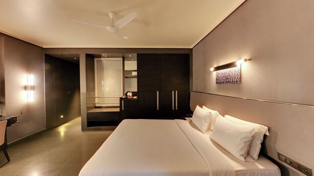 A modern hotel room with a large bed, a wardrobe, a vanity, and a ceiling fan. - Hotel Sankam Residency (Belagavi)