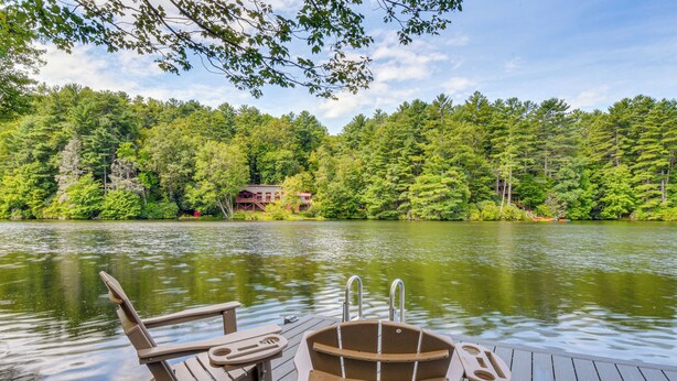 A wooden dock with two Adirondack chairs and a paddle boat, overlooking a lake with dense forest and a cabin in the background. - 4 Mi to Ski Sapphire! Lakefront Cabin w/ Dock (Sapphire)