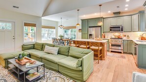 A spacious living room with a green sofa, a coffee table, and a dining area with wooden chairs and a table. The kitchen features green cabinets, a microwave, and a stove. - 4 Mi to Ski Sapphire! Lakefront Cabin w/ Dock (Sapphire)